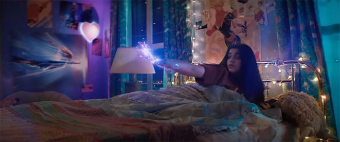 Kamala Khan raises her right hand to create a light construct while a Terry Dodson illustration of Captain Marvel is visible in the background.